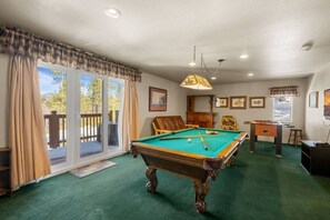 A pool table in a room with a green carpet, a wooden chair, and a table tennis table. - Steps 2 Summit - Walk to Slopes, Pool Table (Big Bear Lake)