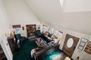 A loft-style living room with a fireplace, green armchairs, a dark leather sofa, and a large window. - Steps 2 Summit - Walk to Slopes, Pool Table (Big Bear Lake)
