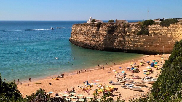 Una playa con barcos, sombrillas y un acantilado con edificios.