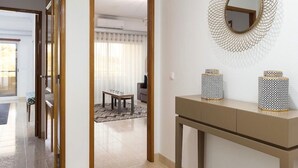 Un pasillo con una puerta que da a un comedor, un espejo con marco decorativo y dos jarrones estampados sobre una consola.