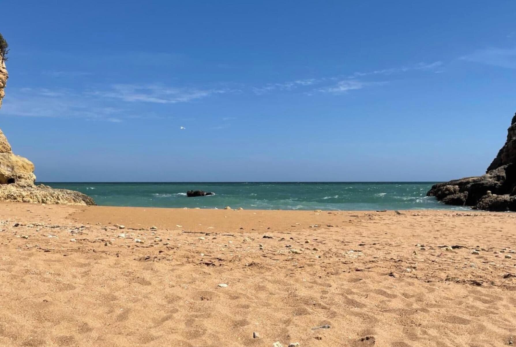 A beach with clear skies, a sandy shore, and rocky cliffs.