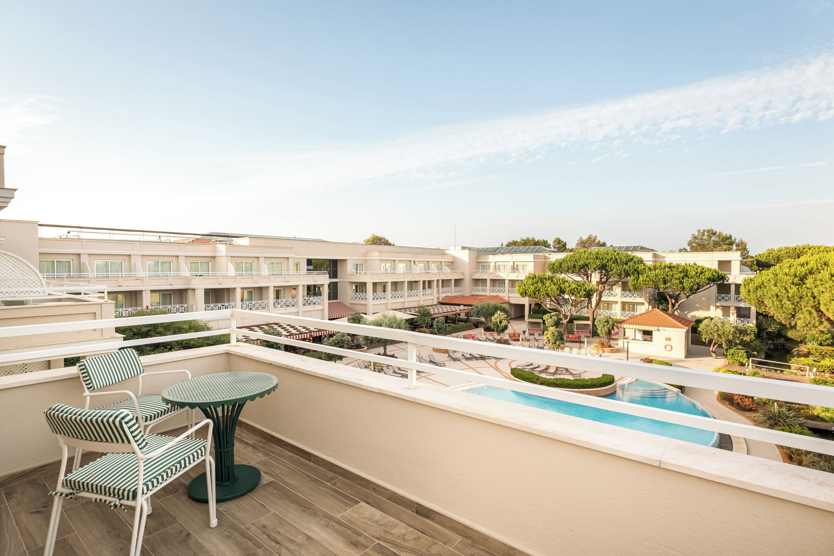 En hotelbalkon med pool, liggestole og udsigt til de omkringliggende bygninger.