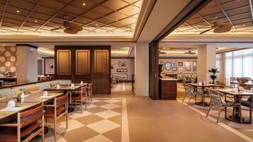 A spacious hotel lobby with a checkered floor, multiple dining areas, and ceiling fans.
