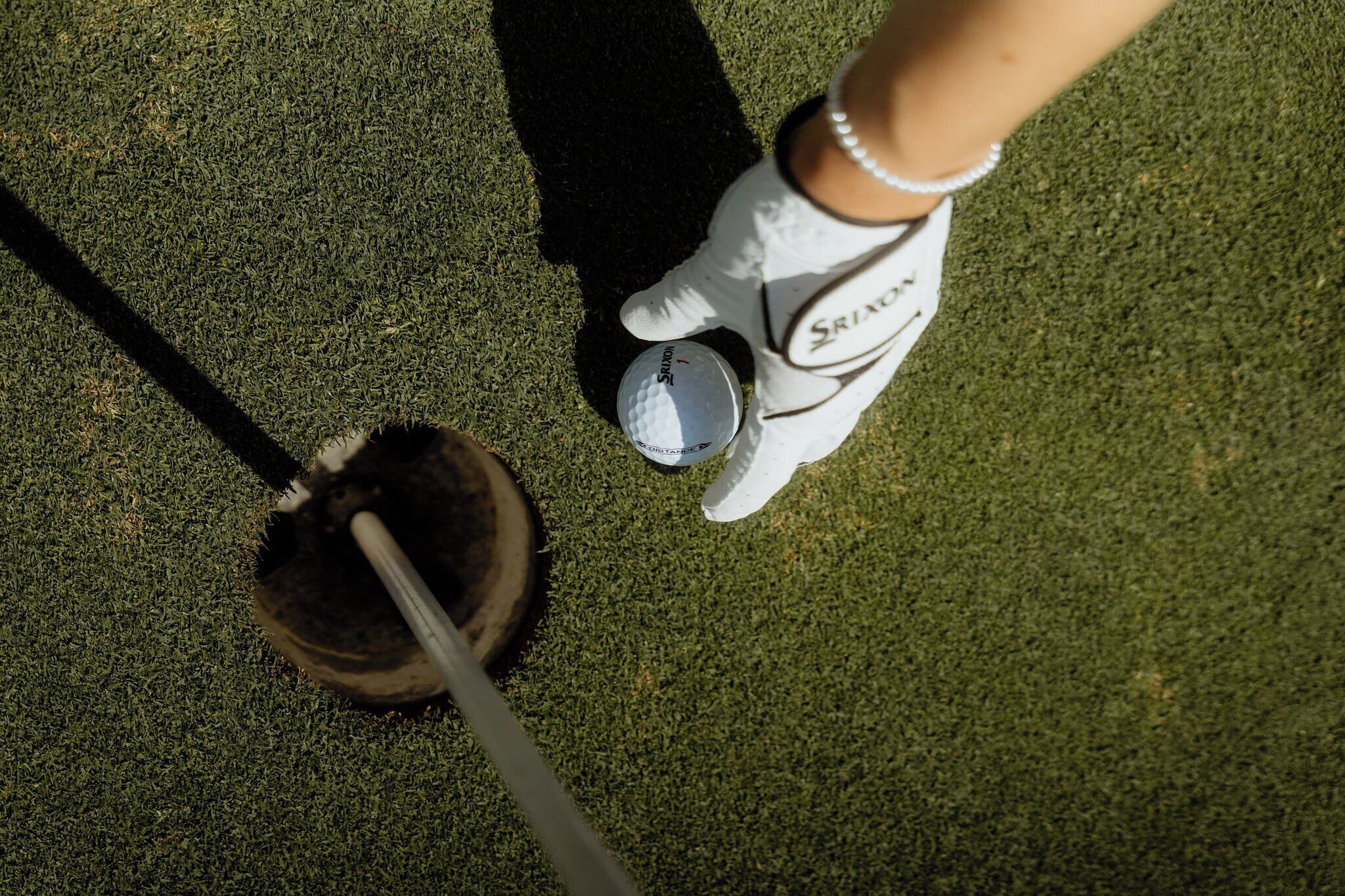 A golf club on a green with a golf ball and a glove.