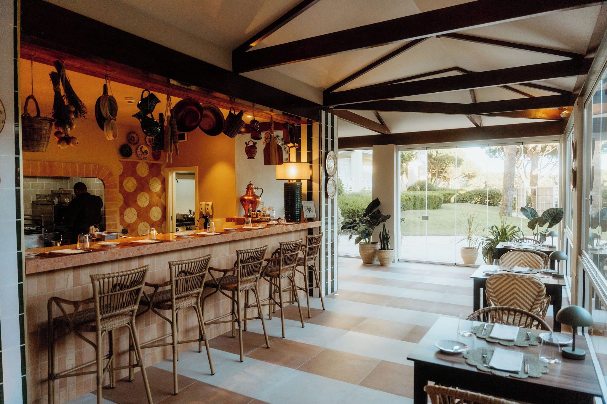 A restaurant with a bar area, wicker chairs, and a view of the garden.