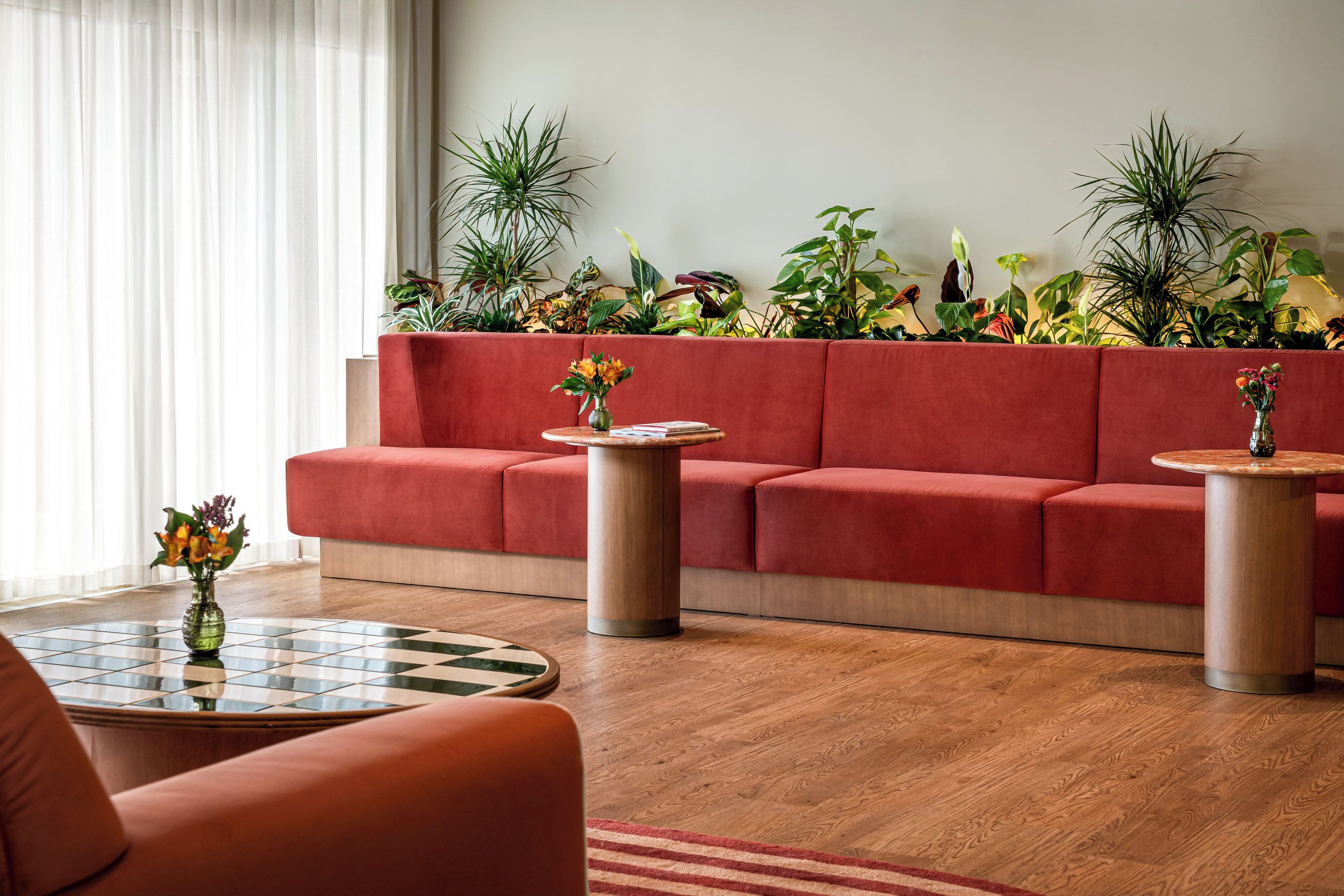 A modern living room with a red sofa, two round tables, and a variety of plants.