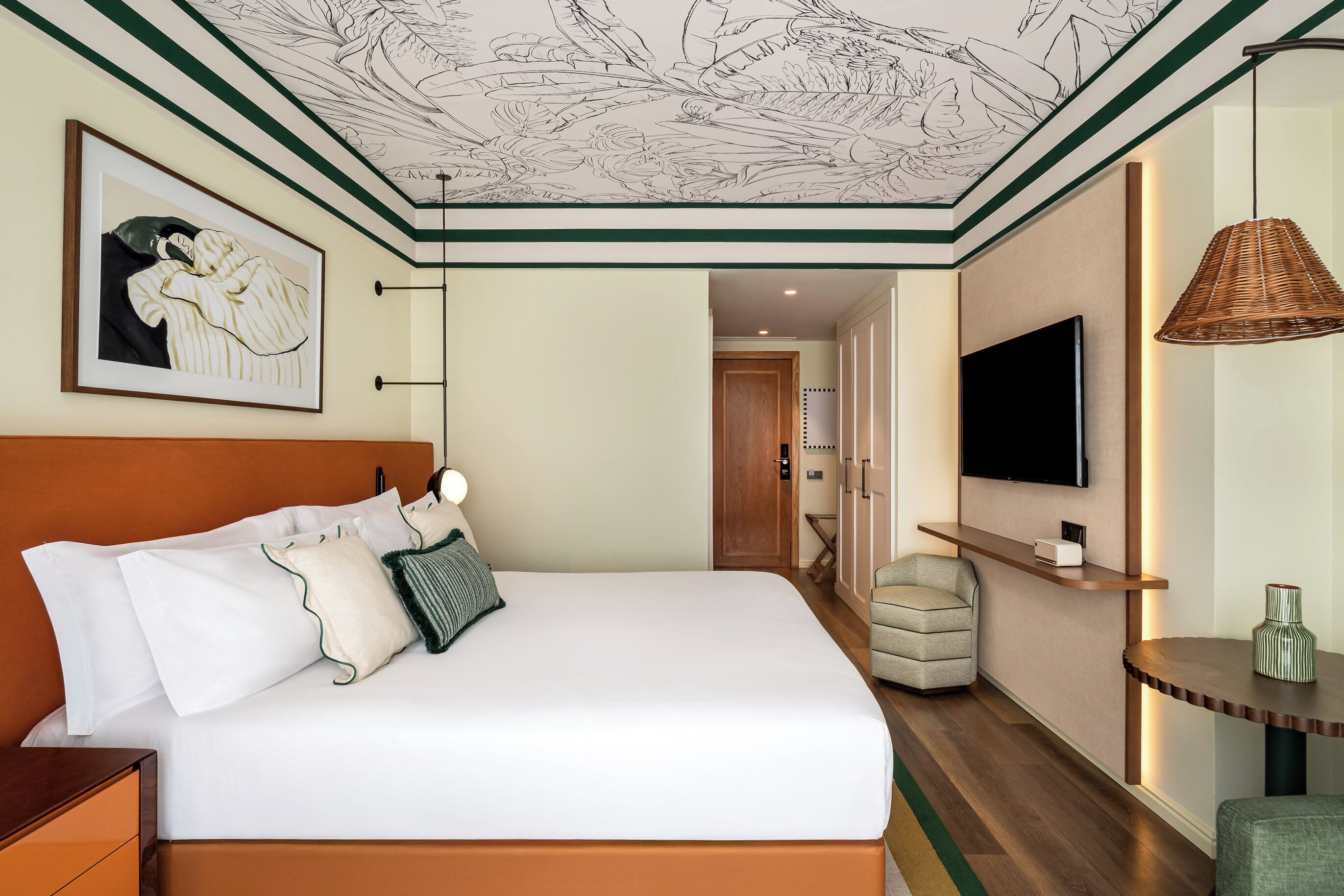 Een hotelkamer met een groot bed, een televisie, een rieten lamp en een ingelijst kunstwerk aan de muur.