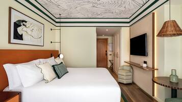 A hotel room with a large bed, a television, a wicker lamp, and a framed artwork on the wall.
