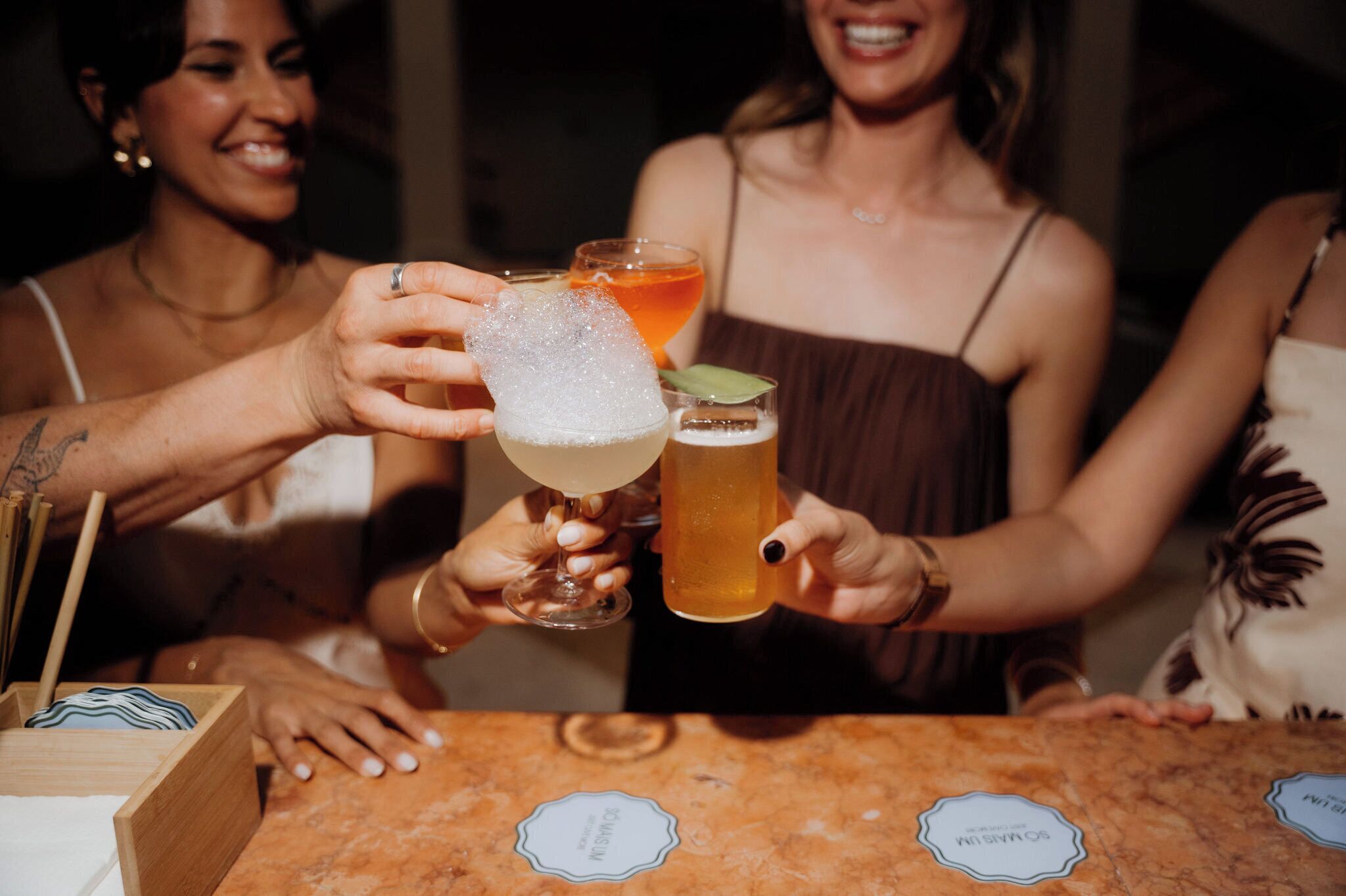 A group of people holding drinks at a bar with a wooden counter and a menu stand.