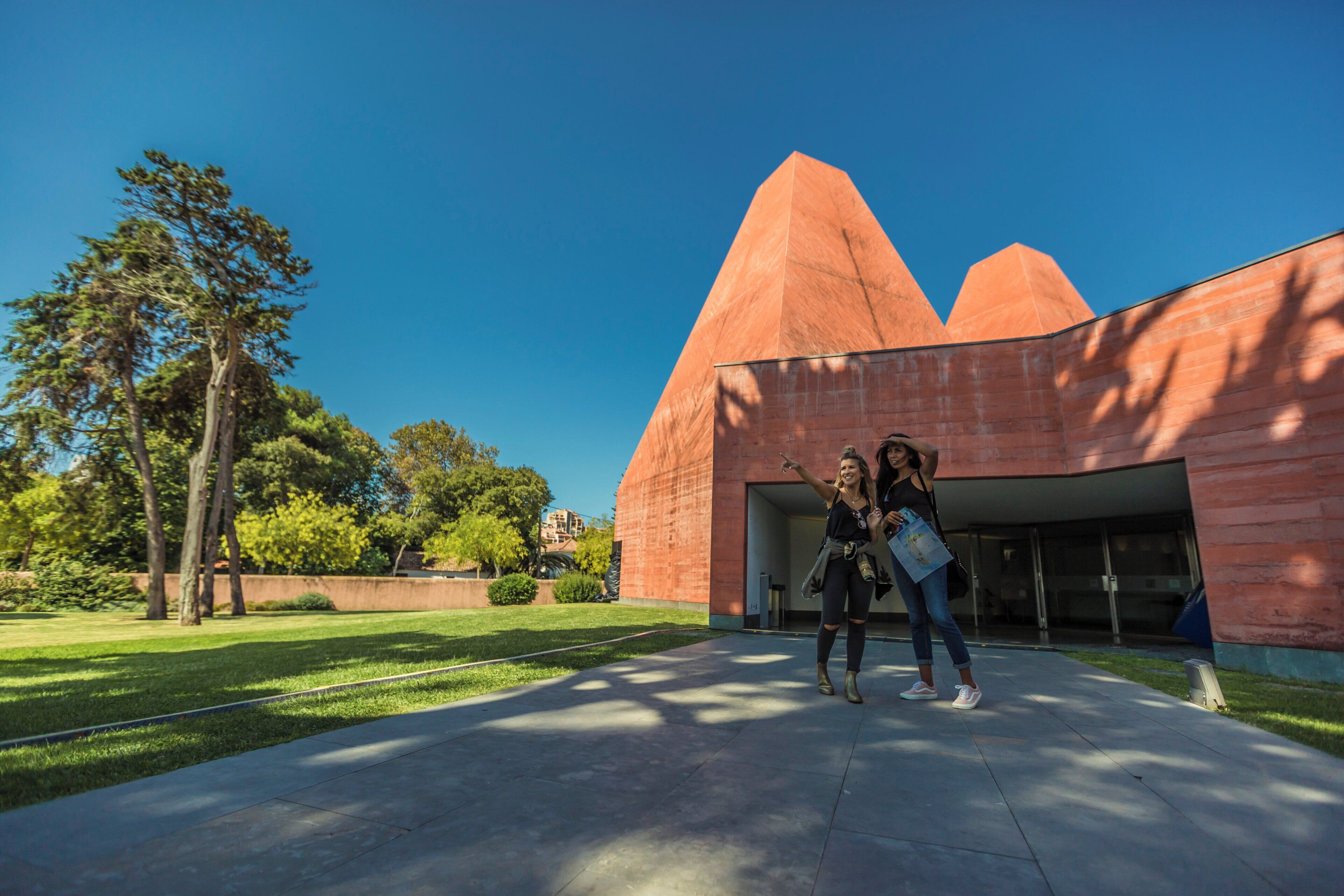 A building with a unique red pyramid-like structure, a paved walkway, and trees in the background.