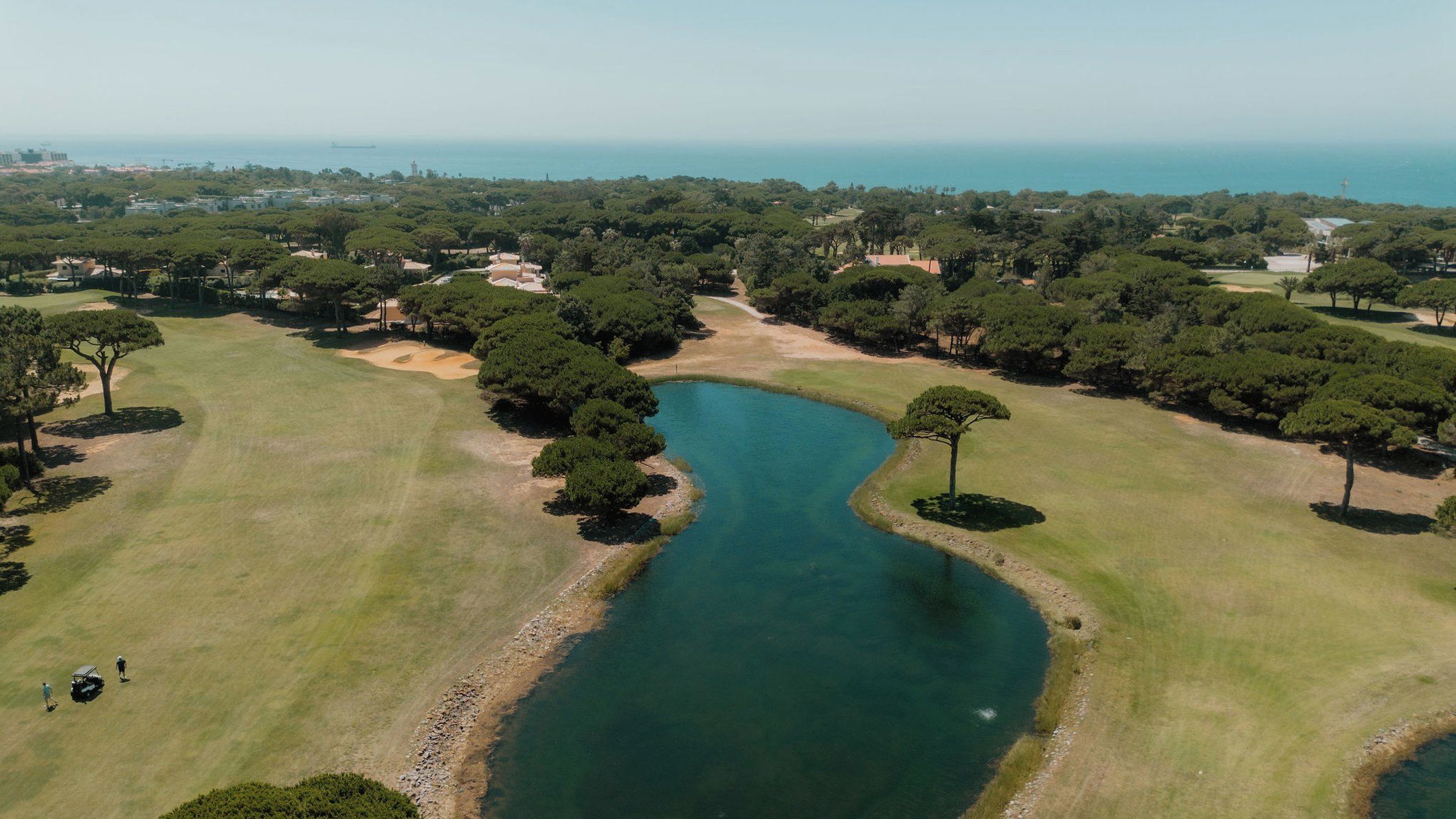 An aerial view of a golf course with a water body, surrounded by trees and open grassy areas.