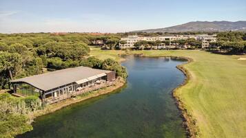 A golf course with a water feature, a building with a covered patio, and a mountainous backdrop.