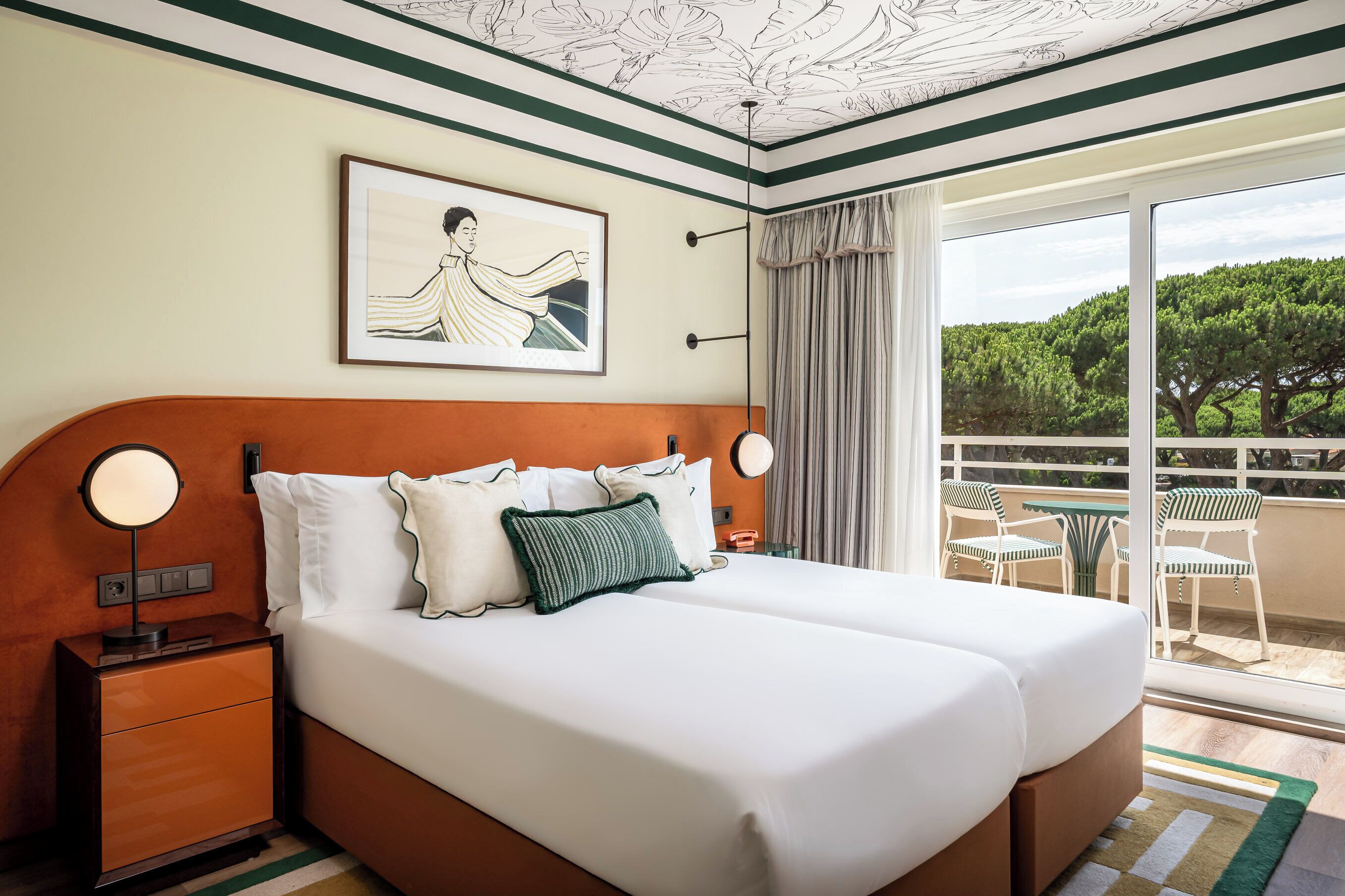 A hotel room with a large bed, two bedside tables, a framed artwork, and a balcony with chairs.