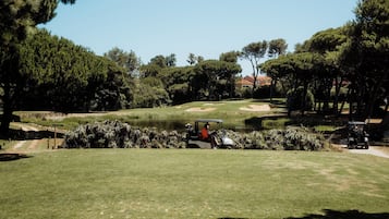 Ein Golfplatz mit Teich, Bäumen und einem Golfwagen.