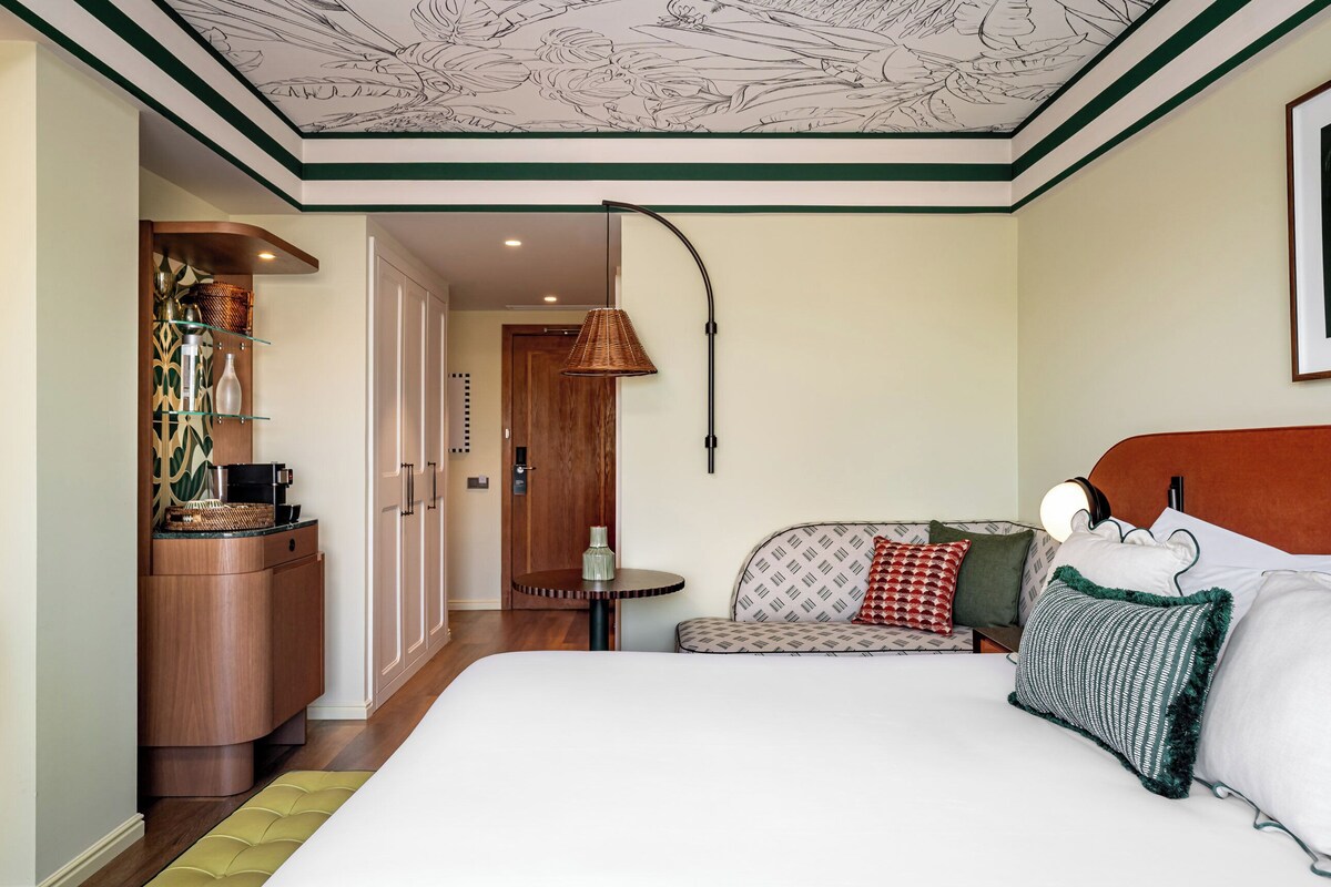 Una habitación de hotel con una cama grande, una mesita de noche, una lámpara, una silla y un armario.