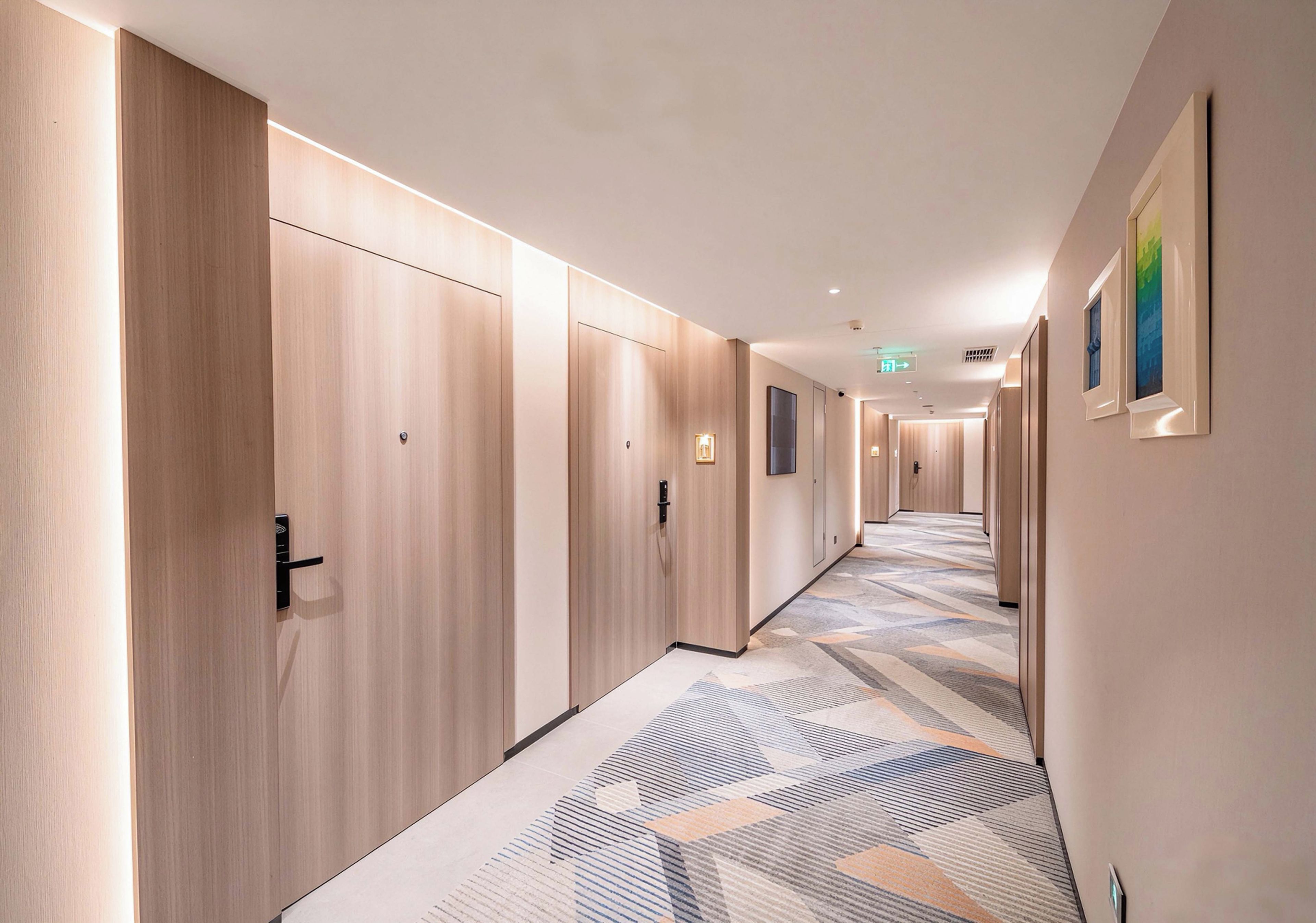 A hotel corridor with wooden doors, a patterned carpet, and framed artwork on the walls.