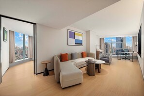 A modern living room with a sofa, ottoman, and coffee table, a desk with a chair, and large windows offering city views. - Holiday Inn Express Chongqing Yangjiaping by IHG (Chongqing)