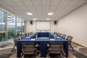 Une salle de conférence dotée d’une longue table, de chaises, d’un écran de projection et offrant une vue sur les bâtiments à travers de grandes fenêtres.