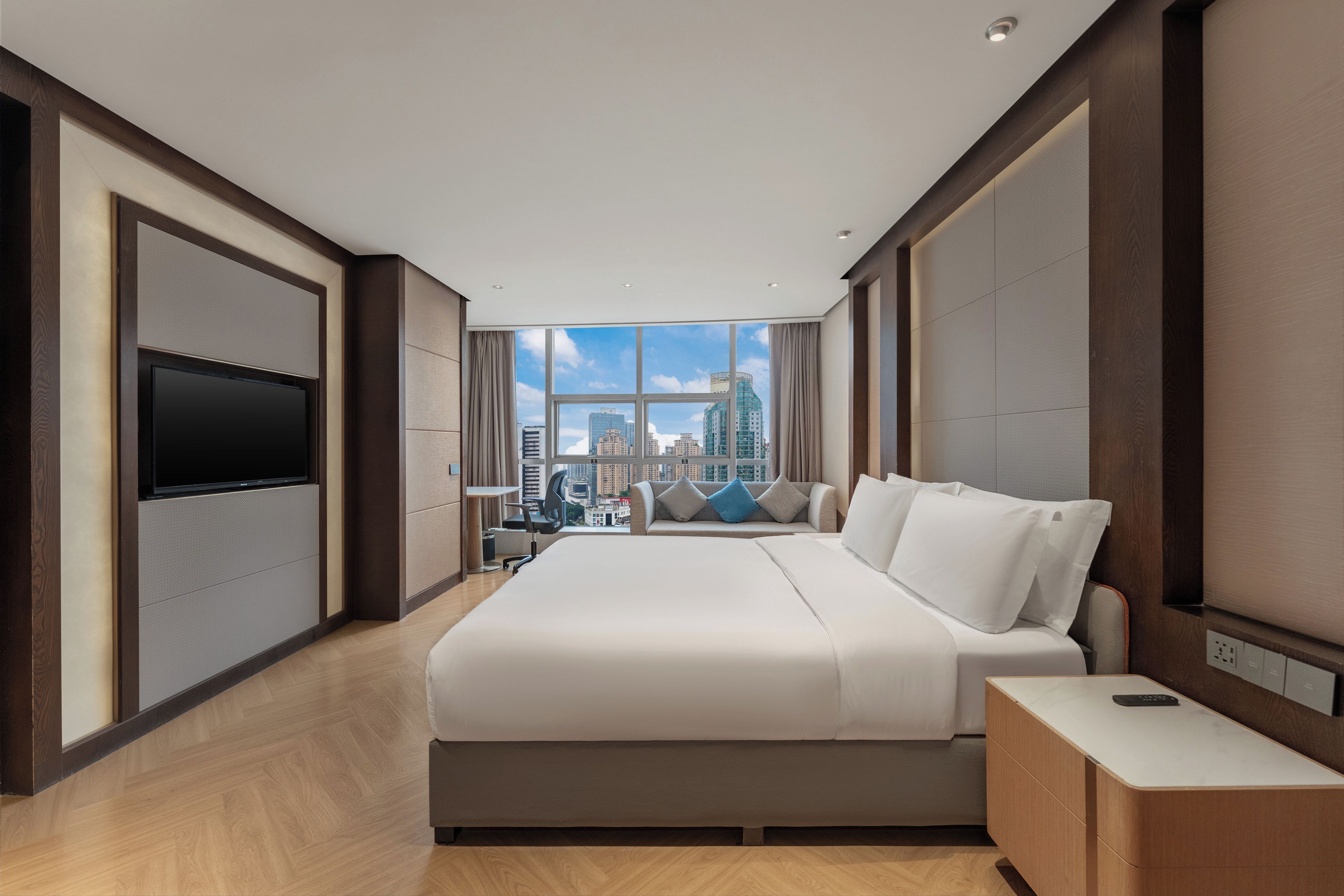 Habitación de hotel moderna con una cama grande, televisión de pantalla plana, escritorio y vistas a la ciudad.