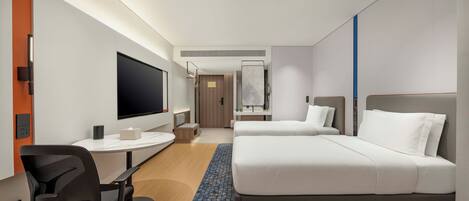 A hotel room with a bed, a desk, a chair, a television, and a bathroom visible in the background.
