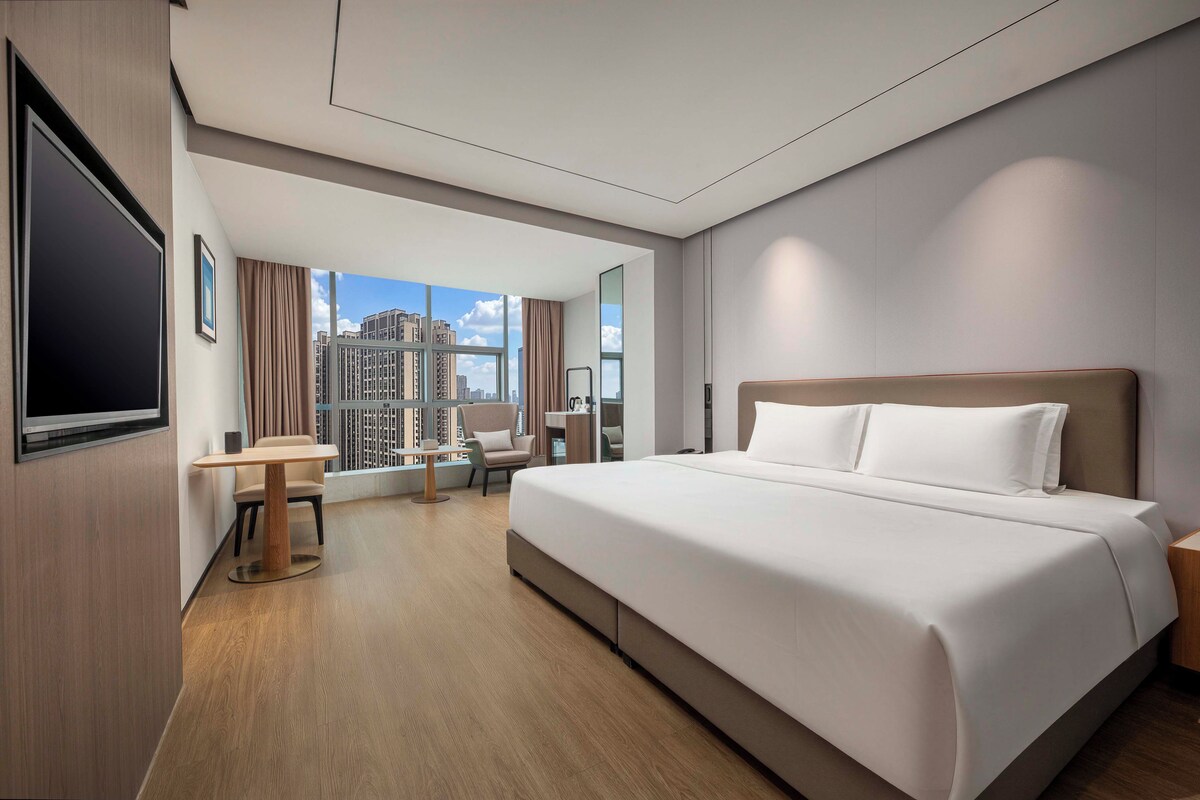 A hotel room with a large bed, a desk, a chair, and a TV.