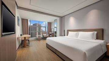 Quarto de hotel com cama grande, escrivaninha, cadeira e televisão.