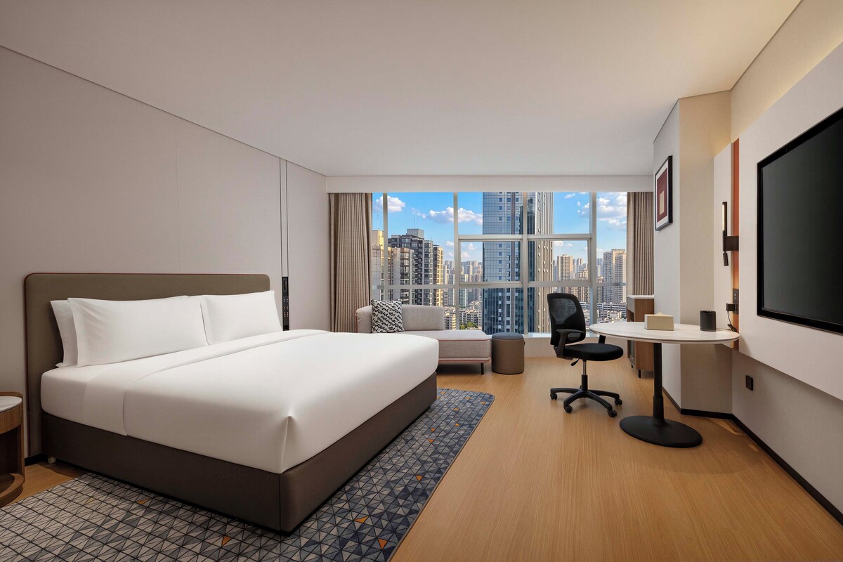 A hotel room with a large bed, a desk, a chair, and a TV.