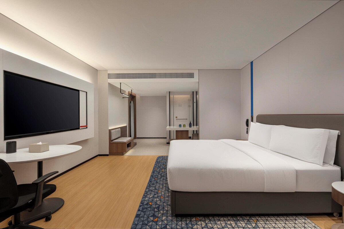 A hotel room with a bed, a desk, a television, and a bathroom visible through an open door.