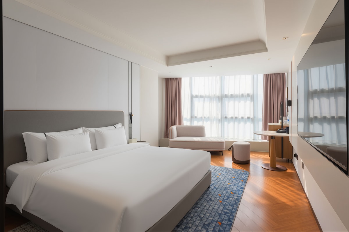 A modern hotel room with a large bed, a seating area, and a large mirror.