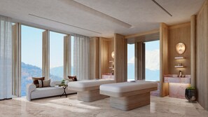 Une chambre d’hôtel moderne dotée d’un grand lit, d’un canapé, d’une table de massage et offrant une vue sur les montagnes.