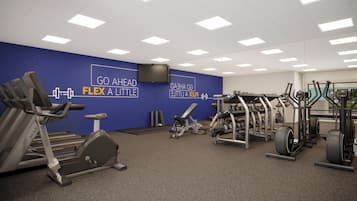 Un gimnasio con diversos equipos de ejercicio, una pared azul con texto motivacional e iluminación empotrada en el techo.
