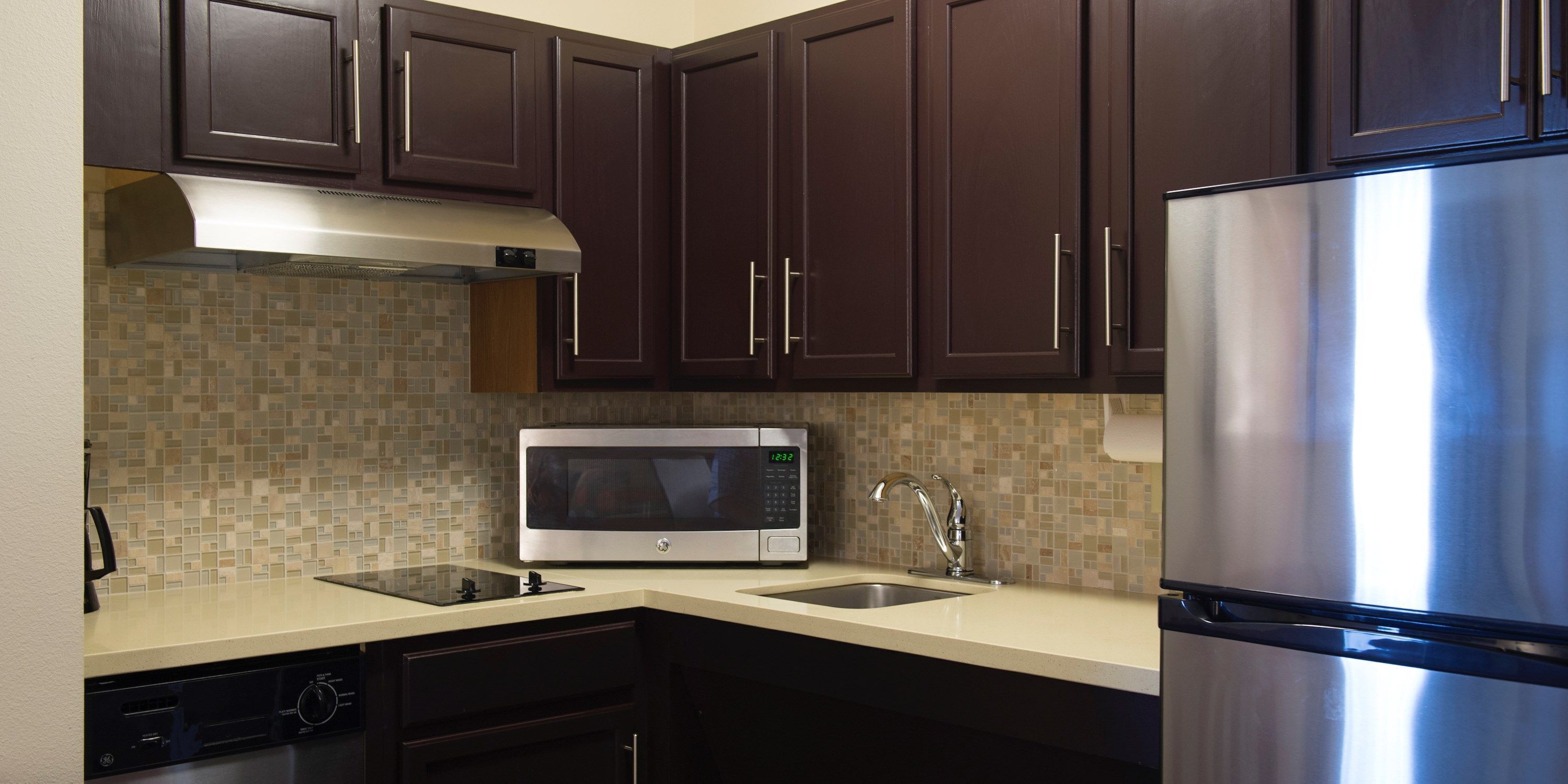 A kitchen with dark brown cabinets, a stainless steel refrigerator, a microwave, a sink, and a dishwasher.