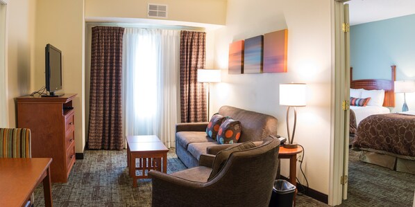 A hotel room with a bed, a desk, a chair, a TV, and a lamp.