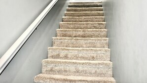 Een trap met een gestructureerd vloerkleed, metalen leuning en een effen muur.