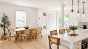 A modern kitchen with white cabinets, a central island, and a dining area with wooden chairs and a table. - Brand New 2026 Villa, 5 min Walk to the Beach, King Canopy Suite, Sleeps 16 (Keansburg)