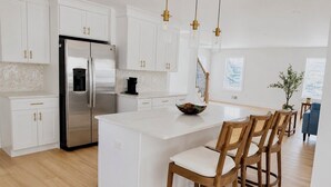 A modern kitchen with white cabinetry, a stainless steel refrigerator, a coffee maker, and a large island with chairs. - Brand New 2026 Villa, 5 min Walk to the Beach, King Canopy Suite, Sleeps 16 (Keansburg)