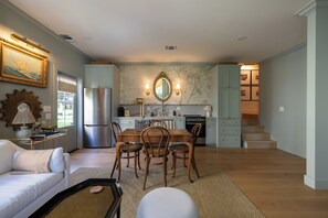 A spacious living area with a dining table, chairs, a sofa, and a kitchen in the background. - Brand New Cottage, Prime Location, Fire Pit! (Fredericksburg)