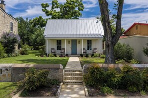 A single-story house with a front porch, a metal roof, and a well-maintained lawn. - Brand New Cottage, Prime Location, Fire Pit! (Fredericksburg)