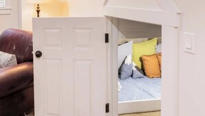 Una habitació amb un llit, una porta que condueix a una altra estança, una làmpada i una catifa amb dibuixos.