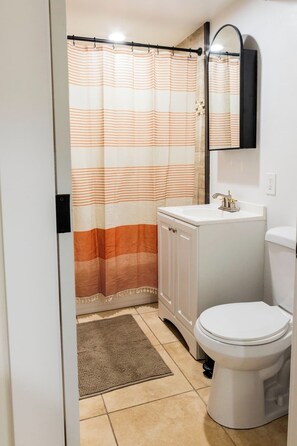 A bathroom with a striped shower curtain, a white sink, a toilet, and a mirror above the sink. - Tramway Base camp: Your home away from home close to the best recreation in Utah (Sandy)