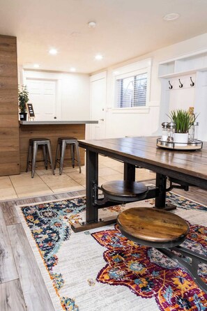 A modern kitchen with a wooden table, stools, and a colorful rug. - Tramway Base camp: Your home away from home close to the best recreation in Utah (Sandy)