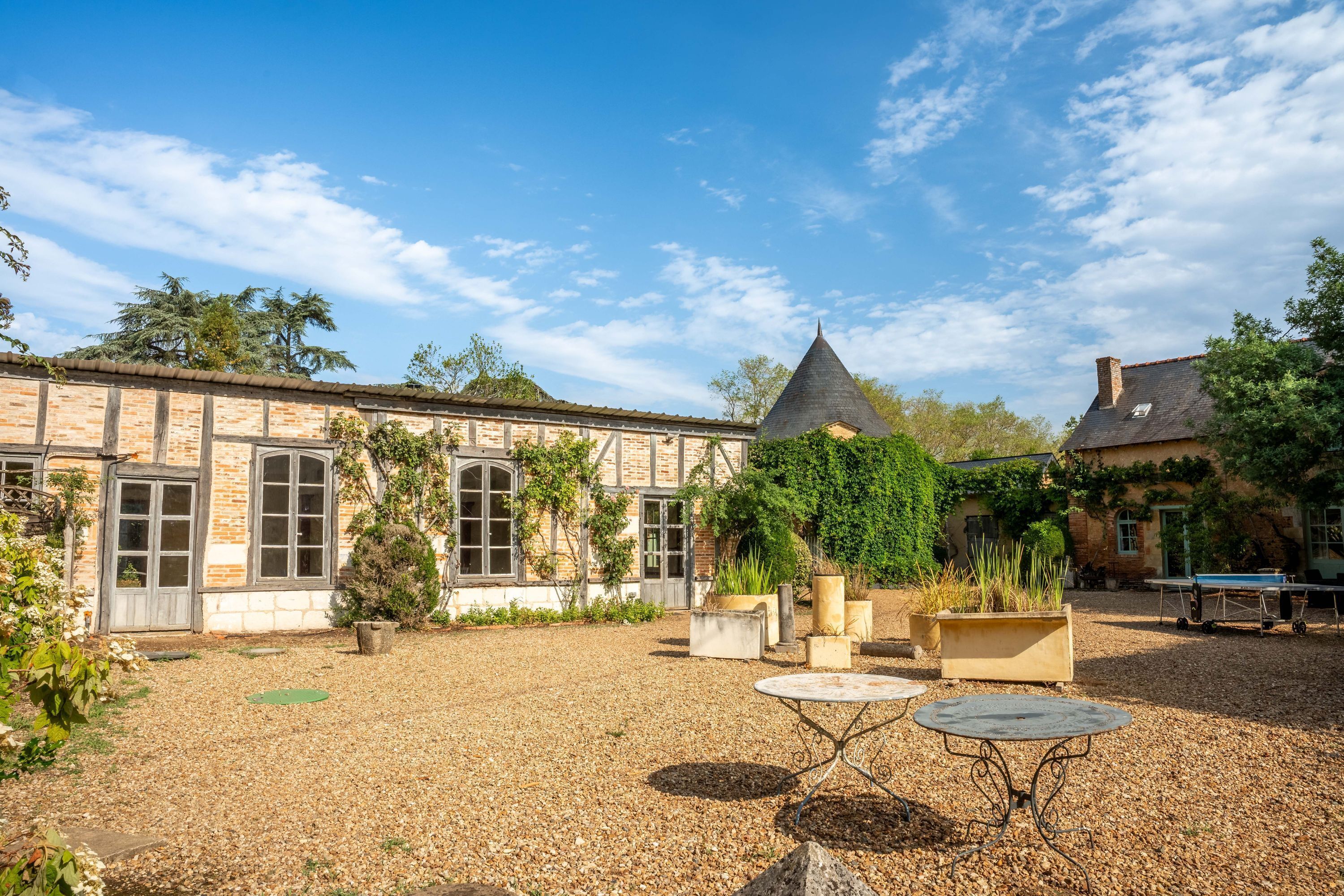 Une cour intérieure avec un bâtiment doté de grandes fenêtres et d’un toit conique, entouré de gravier et de plantes en pot.