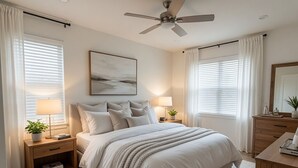 A bedroom with a bed, bedside tables, a ceiling fan, a painting, and a dresser.