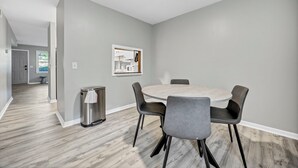 A modern dining area with a round table and four chairs, a trash can, and a kitchen area visible through an open door. - Southern Oasis-Modern Comfort, Minutes from Downtown (Columbia)