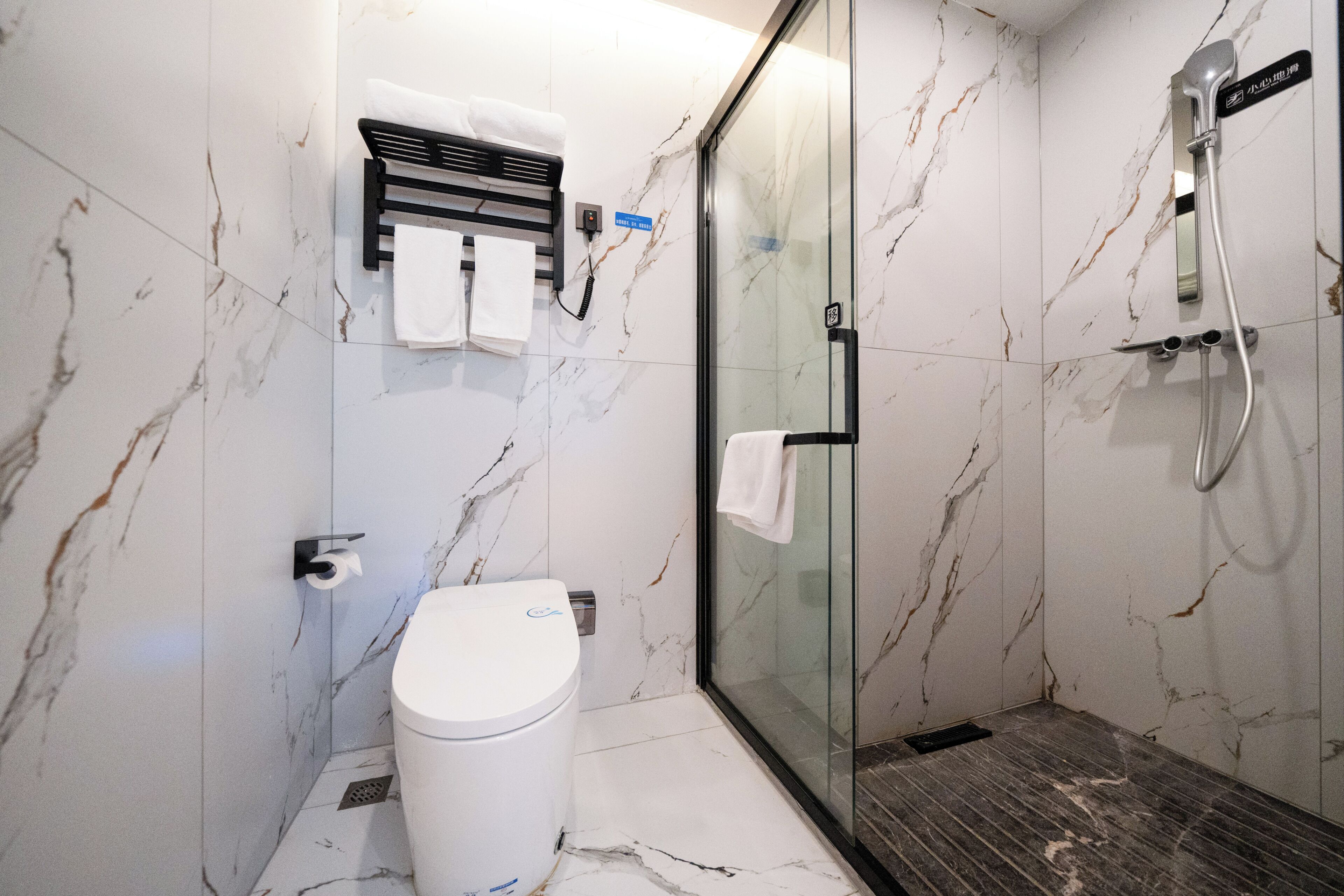 Un baño moderno con inodoro, cabina de ducha de vidrio y pared revestida de mármol.