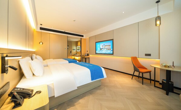 Une chambre d’hôtel moderne équipée d’un lit, d’une table de chevet, d’un bureau, d’une chaise et d’un écran de télévision diffusant une vue sur la ville.