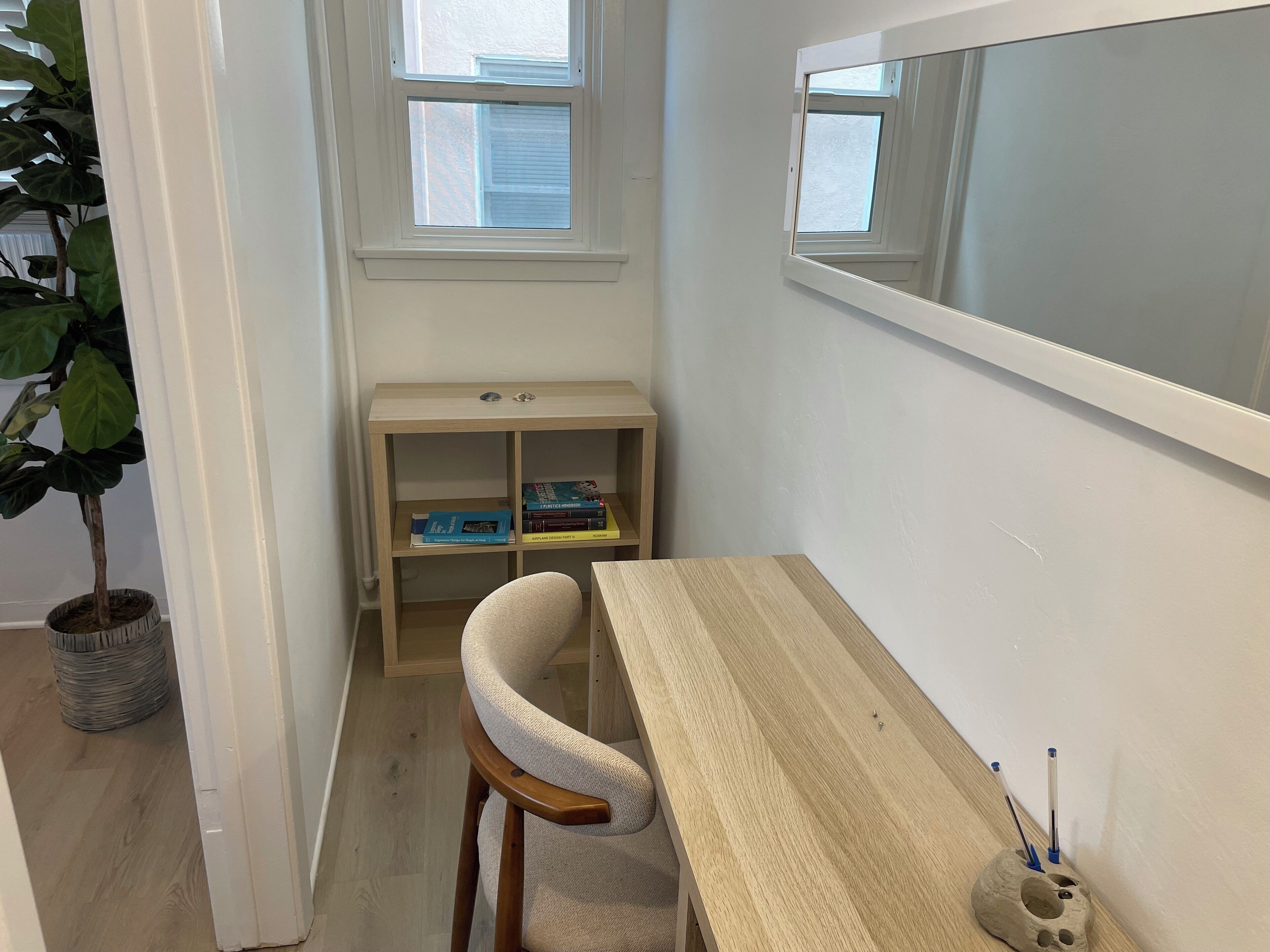 A room with a desk, chair, bookshelf, potted plant, and a large window.