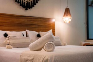 A neatly made bed with rolled white towels, a wooden headboard, and a hanging pendant light. - Xperience Tulum 25 (Tulum)