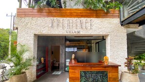 A brick building with a wooden reception desk labeled 'XPERIENCE' and 'TUM' above the entrance. - Xperience Tulum 25 (Tulum)