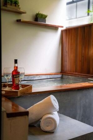 Ein Wellnessbereich mit einer Holzbank, einer Aperol-Flasche, zwei Gläsern und aufgerollten Handtüchern.